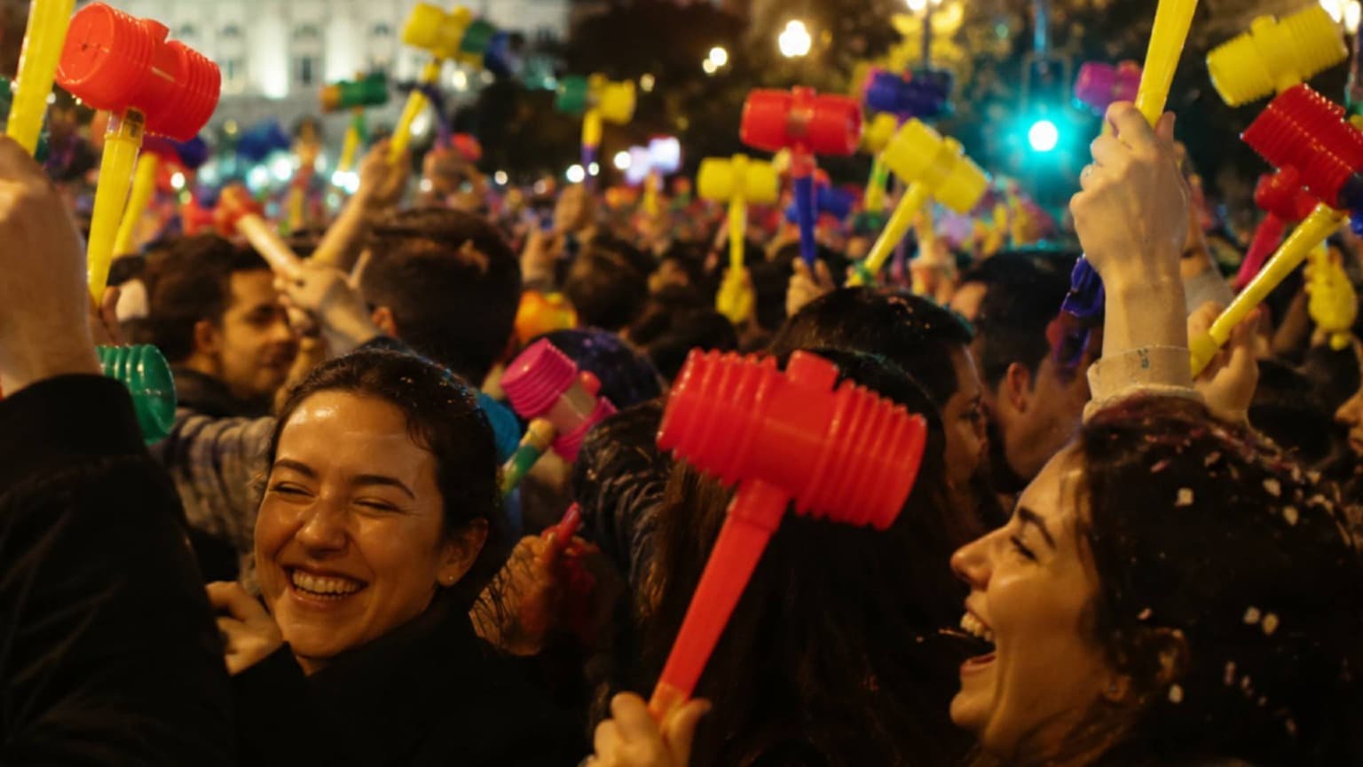 Crowd of people holding colorful plastic hammers during Festas de São João street celebrations in Porto at night