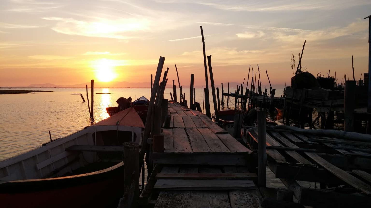 Wooden palafitic pier of Carrasqueira at sunset with traditional fishing boats on calm waters