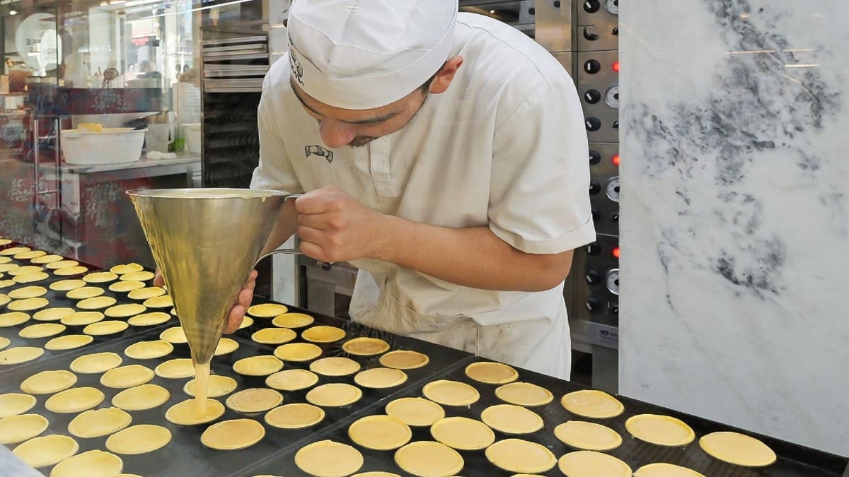 Pastry chef pouring egg custard into tart molds at a bakery in downtown Porto