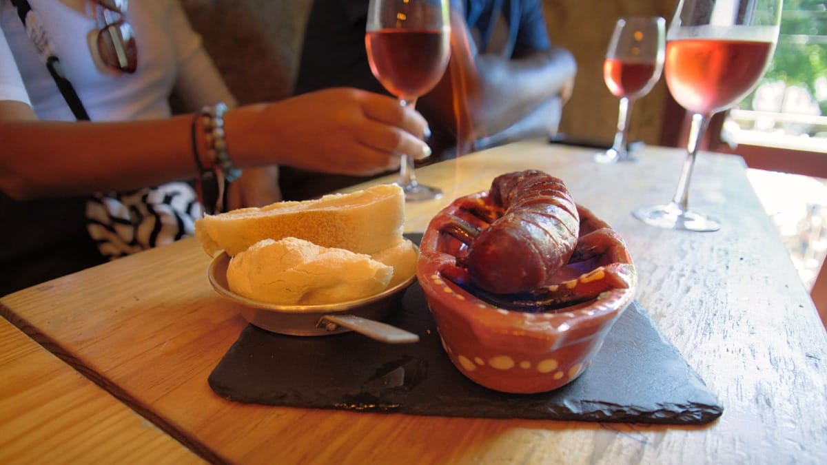 Chouriço tradicional flambado servido com pão e vinho rosé num wine bar do Porto
